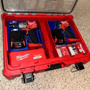 May include: A red Milwaukee tool case with a transparent lid, housing two red and black power drills, two black batteries, and a set of drill bits. The case is open, displaying the tools in an organised manner.