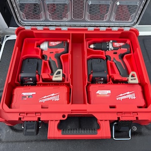 May include: A red Milwaukee hard-shell tool case with a clear lid, containing two power tools, two black battery packs, and two red accessory cases. The tools are a red and black impact driver and a drill driver, both featuring the Milwaukee logo.