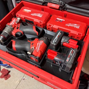 May include: A red toolbox filled with red and black power tools and accessories. The tools include drills, impact drivers, and batteries. The brand name "Milwaukee" is visible on the cases and tools.