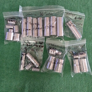 May include: A collection of silver-colored metal socket tools organized into six clear plastic bags. Each bag features handwritten black ink labels detailing specifications such as metric sizes, drive measurements, and V-Series branding.