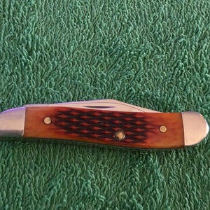 May include: A white ceramic mug with a black handle and the text "But First, Coffee" in a bold, black font. The mug is set against a blurred background, suggesting a cozy setting.