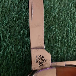 May include: A white ceramic mug with a black handle and the text "But First, Coffee" in a bold, black font. The mug is set against a blurred background, suggesting a cozy setting.