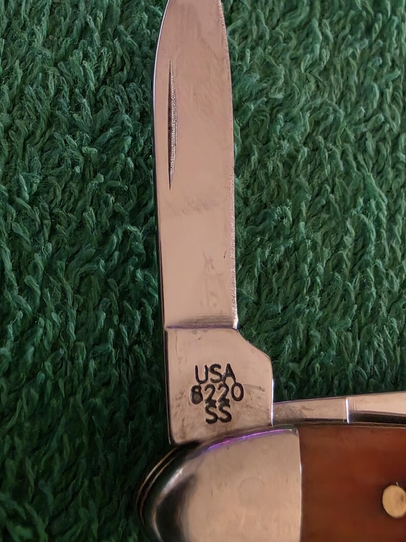 May include: A white ceramic mug with a black handle and the text "But First, Coffee" in a bold, black font. The mug is set against a blurred background, suggesting a cozy setting.