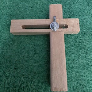 May include: A wooden circle cutter tool with a metal fastener. The tool is made of light-colored wood and has a cross-shaped design. The cutter is designed for making circles in various materials.