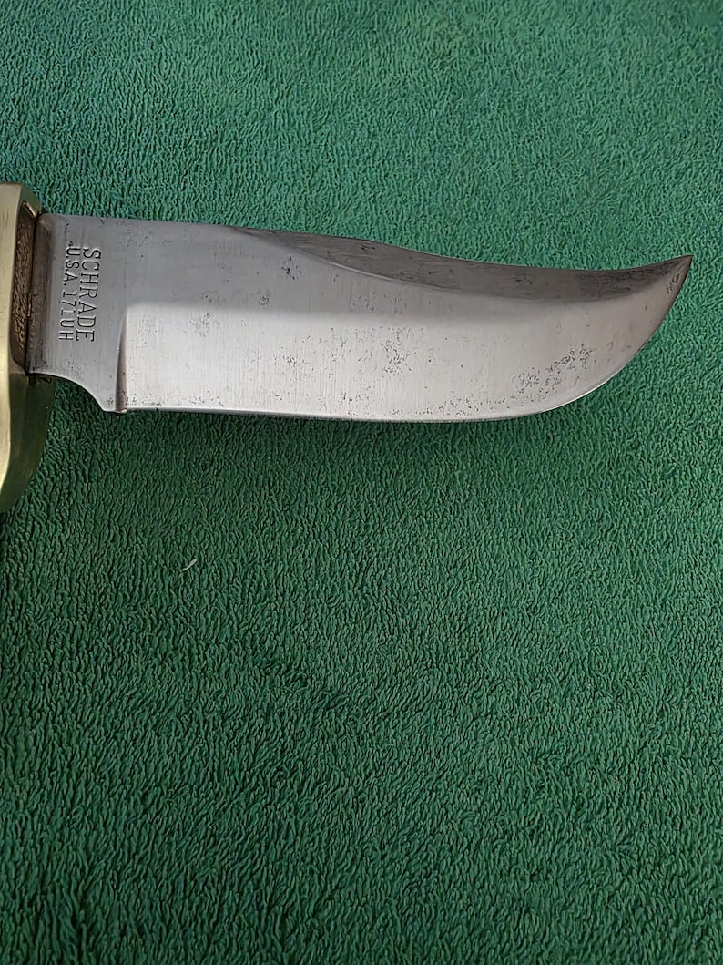 Pu&ograve; includere: Primo piano di una lama di coltello argentata con il testo "SCHRADE USA 177UH" sul lato.