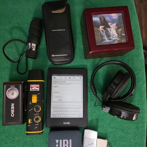 May include: A collection of items including a black monocular, a black Seiko Instruments case, a wooden box with an eagle and waterfall print, a Nebo flashlight, a Marlboro radio, a Kindle e-reader, black headphones, a JBL speaker, and a silver lighter.