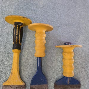 May include: Three hand tools with yellow circular hand guards and textured grips. The left tool is black and yellow with the text STANLEY FATMAX. The middle and right tools have blue metal shafts and yellow handles with a ridged, ergonomic design.