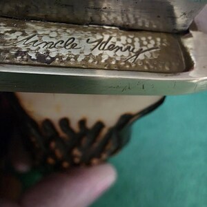 Pu&ograve; includere: Primo piano di un'iscrizione in ottone su un manico di coltello. L'iscrizione recita "Uncle Henry".