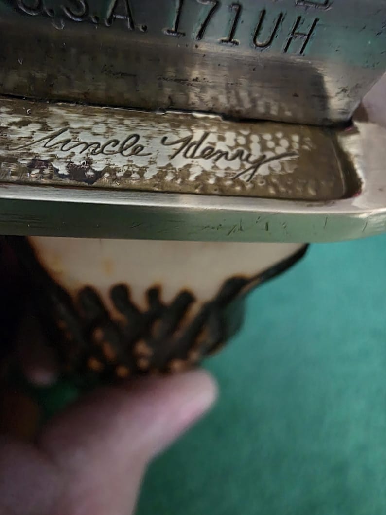 Pu&ograve; includere: Primo piano di un'iscrizione in ottone su un manico di coltello. L'iscrizione recita "Uncle Henry".