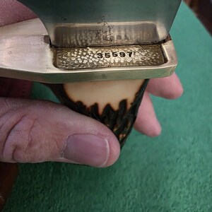 Pu&ograve; includere: Primo piano di un manico di coltello con una guardia in ottone e un manico in corno di cervo. La guardia ha il numero 35597 inciso.