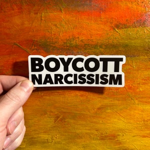 May include: White sticker with black text that reads "BOYCOTT NARCISSISM".