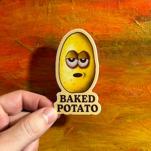 May include: A sticker featuring a cartoon baked potato with sleepy eyes and the text "BAKED POTATO" in brown. The potato is yellow with brown shading and a light beige border. The background is an abstract blend of orange and yellow.