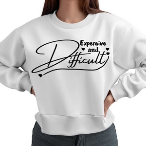 May include: White sweatshirt with black text that reads "Expensive and Difficult" with a heart symbol on either side of the word "and".