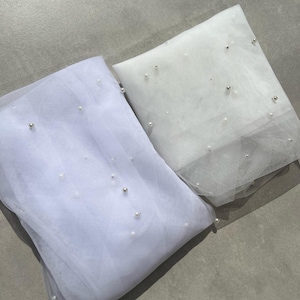 Puede incluir: Dos telas de tul blanco con adornos de perlas. La tela de la izquierda es de un tono blanco m&aacute;s claro y tiene una textura m&aacute;s delicada. La tela de la derecha es de un blanco m&aacute;s brillante y tiene una textura m&aacute;s robusta.