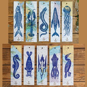May include: A set of ten rectangular bookmarks featuring blue ink illustrations of marine life including a fish skeleton, lobster, eel, whale, jellyfish, seahorse, seal, bird, squid, and cormorant, all printed on nautical map backgrounds with an anchor icon.