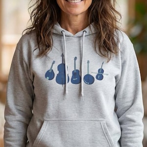 May include: A light gray hoodie with a front pocket and a drawstring hood. The hoodie features a dark blue graphic of various stringed instruments. The person in the image is smiling and looking at the camera.