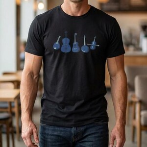 May include: Black t-shirt featuring a blue graphic of stringed instruments, including a banjo, guitar, and violin. The instruments are arranged in a row across the chest. The person is wearing blue jeans.