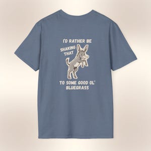 May include: A blue t-shirt featuring a cartoon donkey illustration. The text reads "I'd rather be shaking that to some good ol' bluegrass". The design is in a vintage style, with a playful and humorous theme.