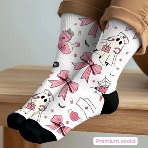 May include: White socks with black heels and toes, decorated with pink bows, medical illustrations, and ghost characters dressed as nurses. The socks have a playful design with a medical and Halloween theme.