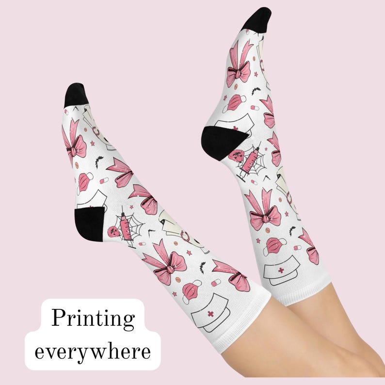 May include: White crew socks featuring a repeating pattern of pink bows, medical caps, syringes with spiderwebs, small pills, and black bats. The socks have solid black heels and toes. The text Printing everywhere is visible in the lower left corner.
