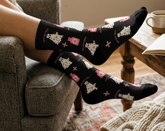 May include: Black socks with a repeating pattern of a ghost, a pink bottle, and a white cross. The text "BOO DOO CREW" is printed on the socks. The socks are worn by a person sitting in a chair.