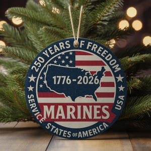 May include: A round, patriotic ornament with a rope hanger. The design features the American flag, a map of the USA, and the text "250 YEARS OF FREEDOM" and "MARINES STATES OF AMERICA". The years "1776-2026" are also displayed.
