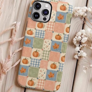 May include: A smartphone case featuring a patchwork design of alternating squares in muted peach, sage green, and blue gingham patterns. The surface is decorated with illustrations of orange pumpkins and brown autumn leaves, with small floral accents.