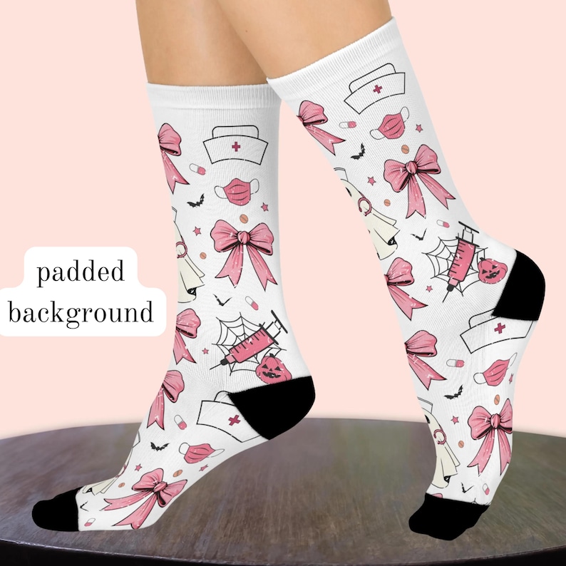 May include: White crew socks featuring a repeating pattern of pink bows, medical caps with red crosses, pink face masks, syringes with spider webs, small pumpkins, pills, and tiny black bats. The socks have solid black heels and toe sections.