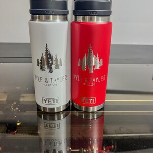 May include: Two stainless steel Yeti water bottles, one white and one red, with black handles. Each bottle features a forest design and the names "KYLE & TAYLER" with the date "10.12.24". The Yeti logo is visible.