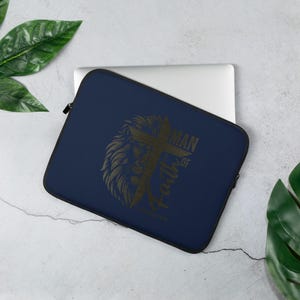May include: A navy blue laptop sleeve with a black lion and cross graphic. The text "Man of Faith" is printed on the sleeve.