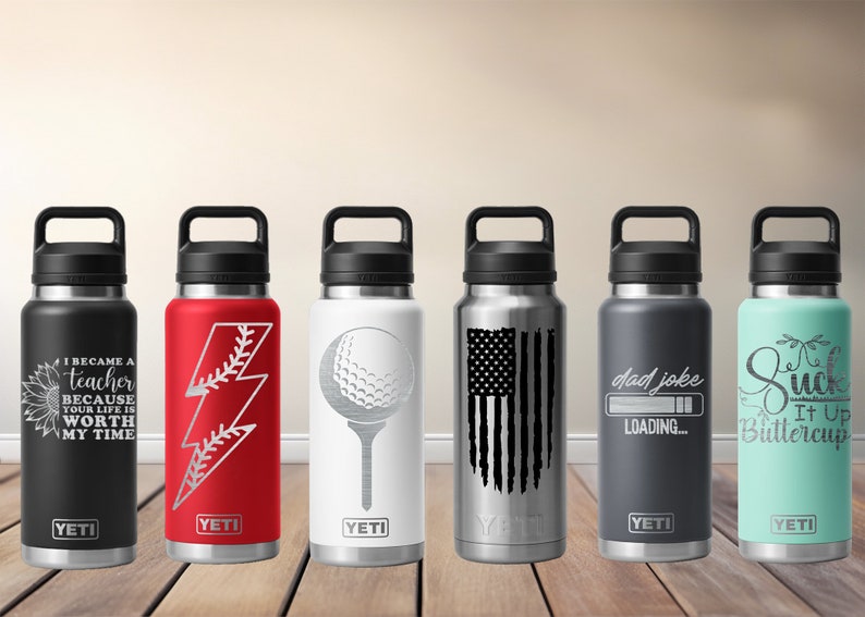 May include: Six insulated water bottles with black handles and lids. Designs include a sunflower with text, a baseball lightning bolt, a golf ball, an American flag, the words "dad joke loading," and the phrase "Suck It Up Buttercup."