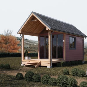 Puede incluir: Una pequeña cabaña de madera roja con un porche cubierto y un techo negro. La cabaña tiene grandes ventanas y una puerta de madera. La cabaña está rodeada de hierba verde y árboles.