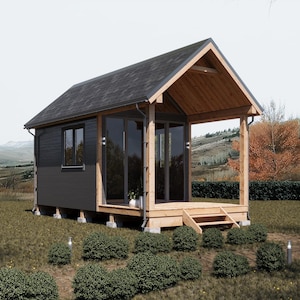 May include: A small, modern cabin with a dark gray exterior and a wooden porch. The cabin has large glass doors and windows, a dark gray roof, and is set in a grassy area with a mountain backdrop.