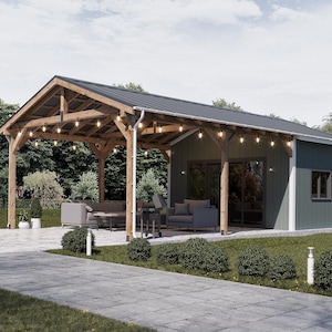 May include: A wooden pergola with a dark metal roof is attached to a green-sided building. The pergola has string lights and is furnished with gray sofas and a table. A paved walkway leads to the structure.