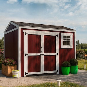 Puede incluir: Un cobertizo de almacenamiento rojo con molduras blancas, techo negro y puertas dobles. Una pequeña ventana es visible en el lateral. El cobertizo está rodeado de vegetación, incluyendo plantas en macetas y una jardinera de madera. Un pequeño cubo de pintura está cerca.
