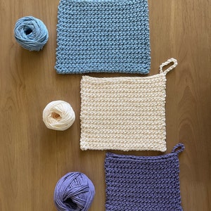 Può includere: Tre strofinacci all'uncinetto in blu, crema e viola, con gomitoli di lana abbinati.
