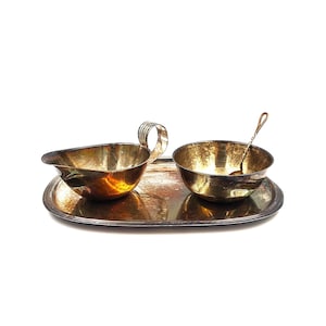 Puede incluir: Un juego de servir de tono plateado vintage. Incluye una salsera con asa, un cuenco pequeño con cuchara y una bandeja ovalada. El juego tiene un aspecto antiguo deslustrado, con desgaste y decoloración visibles.
