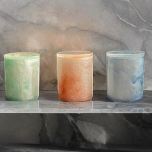 May include: Three cylindrical containers with a marbled, iridescent finish. The containers are green, orange, and blue.