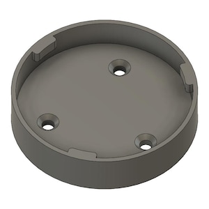 May include: A gray, circular object with a recessed interior and three evenly spaced holes. The outer rim has three rectangular cutouts. The object appears to be made of plastic or a similar material.