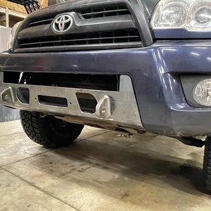 Puede incluir: Un Toyota 4Runner azul con un parachoques delantero personalizado. El parachoques está hecho de metal y tiene un acabado en polvo negro. Cuenta con un soporte de cabrestante y una placa de deslizamiento.