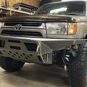 Puede incluir: Un Toyota 4Runner plateado con un parachoques delantero personalizado y neumáticos grandes todoterreno. El parachoques tiene un soporte de cabrestante y una placa de deslizamiento.