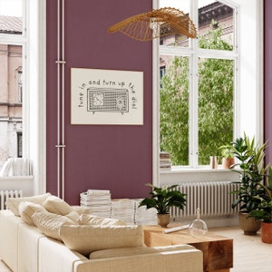 May include: A black and white illustration of a vintage radio with the text "tune in and turn up the dial" on a cream background. The illustration is framed and hanging on a burgundy wall.
