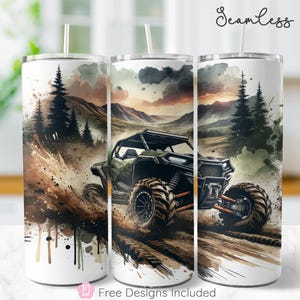 May include: White tumbler featuring a watercolor design of a green off-road vehicle driving through mud, with a backdrop of mountains and pine trees. The tumbler has a straw and the word "Seamless" is written on the top.
