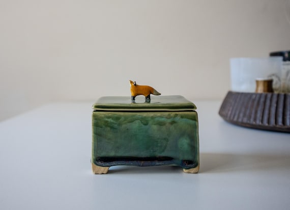 A hand-sculpted ceramic lidded box with a fox — the kind of whimsical, functional art object you'd spot at a craft fair and immediately want.