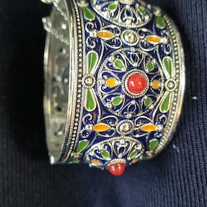 Könnte beinhalten: Ein silbernes Armreif-Armband mit aufwendigen Emaille-Details. Das Armband hat ein lebendiges Design mit blauen, grünen, orangefarbenen und roten Akzenten. Das Armband ist etwa 5 cm breit.
