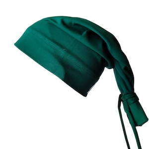 May include: A dark green, soft fabric beanie with a long, tied tail. The beanie is folded over at the top and has a seam running along the fold.