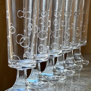 Peut inclure: Un ensemble de six verres à pied transparents. Chaque verre présente un gobelet cylindrique décoré d'un motif de cercles qui se chevauchent. Les verres sont disposés en rangée, mettant en valeur leur design élégant et leur clarté.