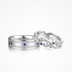 Puede incluir: Dos anillos de plata. Uno tiene piedras preciosas azules y un diseño texturizado. El otro anillo tiene un diseño calado con piedras preciosas claras y azules. Ambos anillos están sobre un fondo blanco.