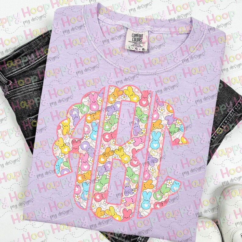 May include: A purple t-shirt with a pink outline of the letters "RY" filled with a pattern of pastel-coloured Peeps candy. The Peeps are arranged in a random pattern and include pink, yellow, blue, and green colours.