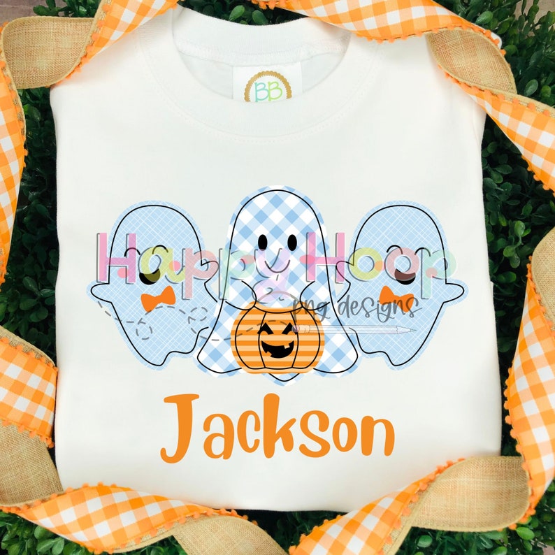 Op de afbeelding: Een wit T-shirt met drie blauwe en witte gingham-geesten die een jack-o-lantern vasthouden. De tekst "Happy Hooligan Designs" staat boven de geesten en de naam "Jackson" staat onder de geesten.